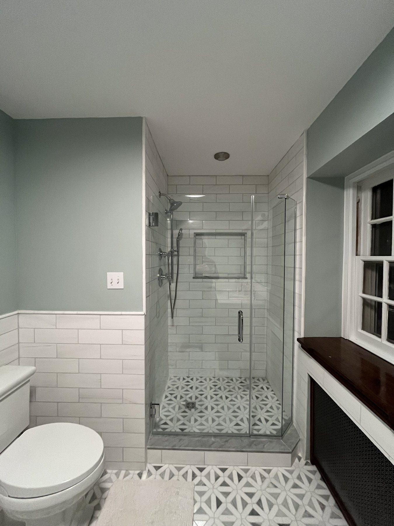 Glass shower enclosure with tiled niche and patterned bathroom floor