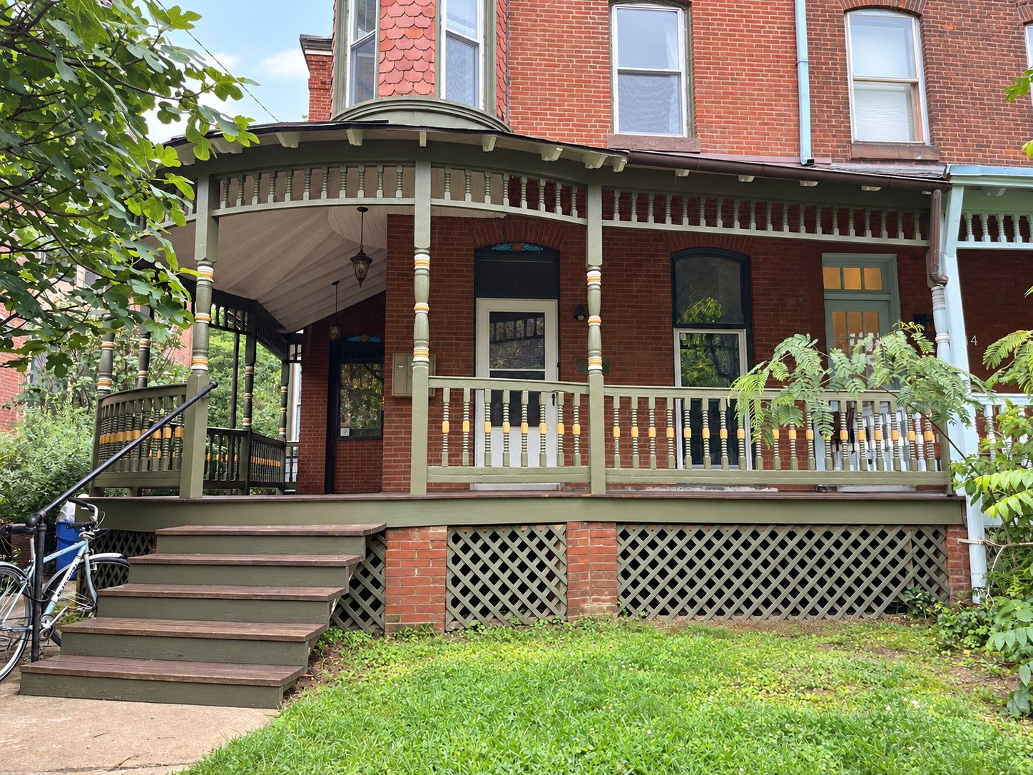 Restored Victorian wraparound porch with painted posts, railings, and gingerbread trim